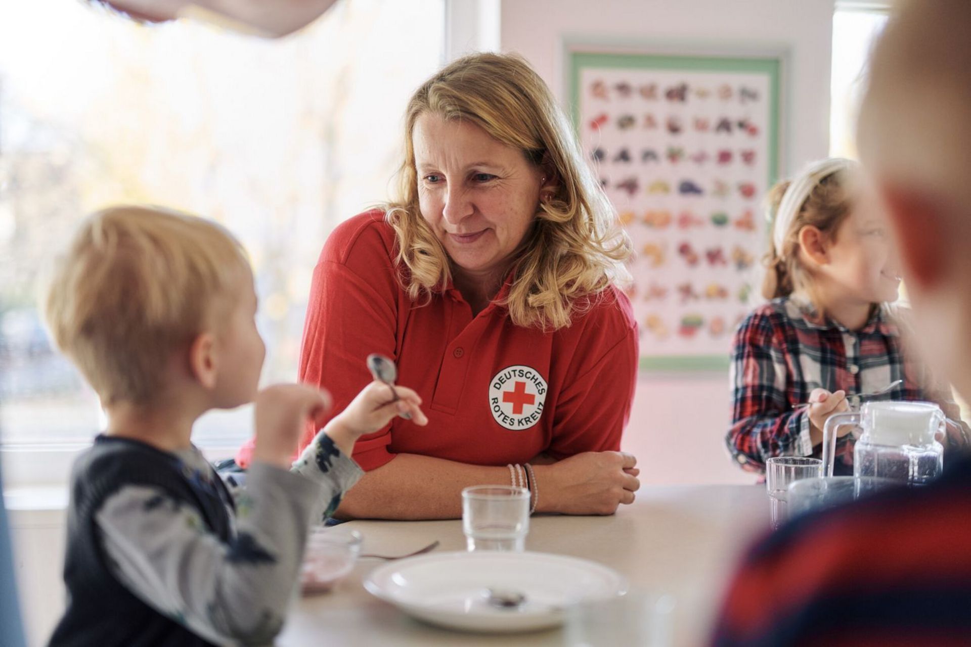 Drei Kinder und eine Erzieherin sitzen am Esstisch.